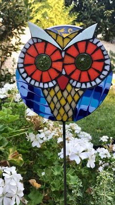 a stained glass owl sitting on top of a metal pole in front of some flowers