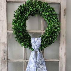 a wreath with a blue and white bow hangs on a door frame in front of an old window