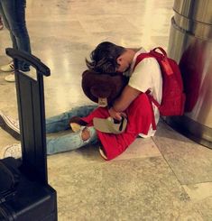 a person sitting on the ground with a teddy bear in their lap and luggage behind them