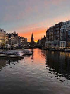 some boats are sitting in the water near buildings and lights at sunset or sunrise time