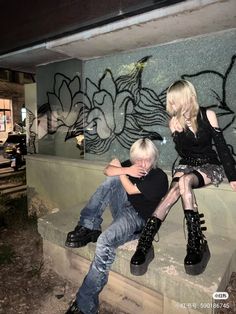 a man and woman sitting next to each other on a cement wall covered in graffiti