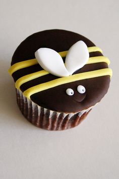 a chocolate cupcake with yellow and white icing on it's side, decorated like a bee