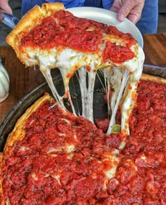 a deep dish pizza with cheese and sauce being lifted from a pan by a spatula