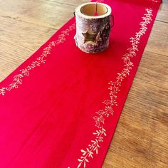 a red table runner with white flowers on it and a candle in a cup next to it