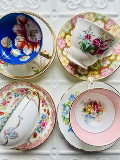 four plates with floral designs on them sitting on a white table top, one has a tea cup and saucer in the middle