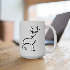 a white coffee mug with a black outline of a deer sitting on top of a wooden table