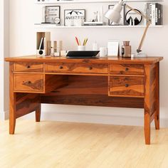 a wooden desk topped with lots of books and office supplies next to a white wall