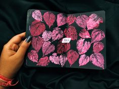 a person holding an open notebook with pink leaves on black paper in front of them