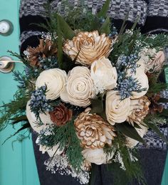 a bridal bouquet with pine cones and greenery in front of a blue door