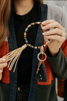 a woman holding a keychain that has beads and tassels on it