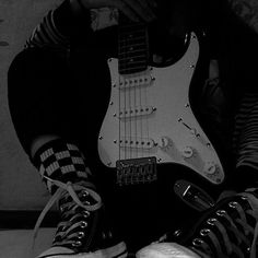 black and white photograph of a person with their legs crossed holding an electric guitar