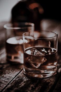 two glasses filled with ice sitting on top of a wooden table