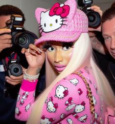 a woman with long blonde hair wearing a pink hello kitty hat and holding a camera