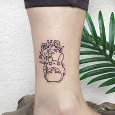 a tattoo on the ankle of a woman with flowers in her hair and a totoro head