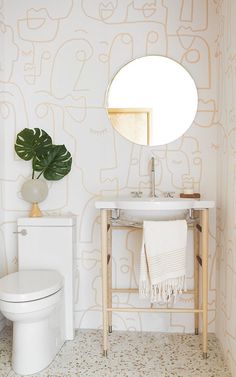 a white toilet sitting next to a sink in a bathroom under a large round mirror