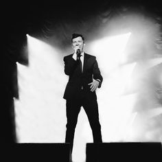 a man in a suit and tie singing into a microphone with his hands on his hips