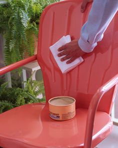 a person is cleaning a red chair with a cloth and a can of paint on it