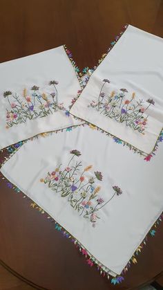 three embroidered napkins with flowers on them sitting on a table