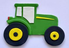 a cookie shaped like a green tractor on a white surface with yellow and black wheels