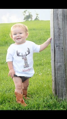 a toddler standing next to a wooden pole in the grass with his hands on it's hips