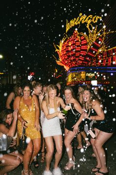 several women are standing in front of a carnival ride at night time with snow falling all around them