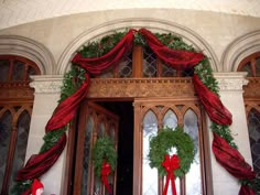 two christmas wreaths on the front door of a building with red ribbons and bows