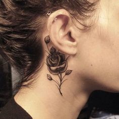 a woman with a black rose tattoo on her left side behind the ear is looking down