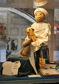 a display case with an old fashioned doll and stuffed animal in it's arms