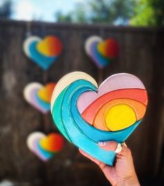 a hand holding a colorful wooden heart shaped object in front of hearts made out of wood