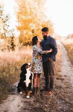 a man and woman standing next to a black and white dog on a dirt road