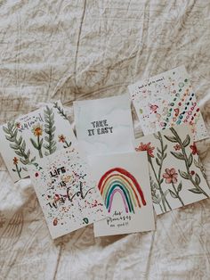 four different cards are laying on a bed sheet and one has a rainbow painted on it