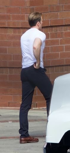 a man in white shirt and black pants standing next to a white car on street