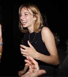 two women laugh as they talk to each other in a dark room with people around them