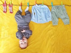 a baby laying on top of a yellow blanket next to clothes hanging from a line