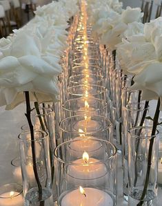 white roses and candles are lined up on a long table with clear glass vases