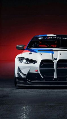 the front end of a white and blue bmw sports car in a dark room with red lighting