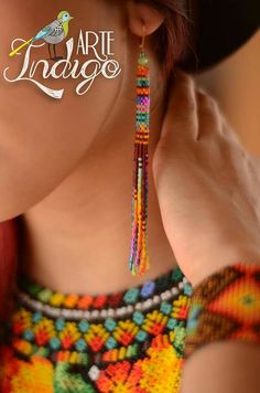 a woman wearing colorful beaded earrings and a black hat with the word art trago written on it