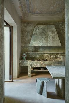 a room with a table, stove and bench in the middle of it that is made out of stone