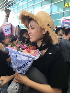 a woman in a straw hat is holding flowers and talking on her cell phone at an airport