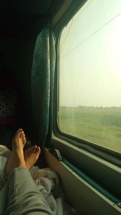 the person is laying down with their feet propped up on the window sill looking out at an open field