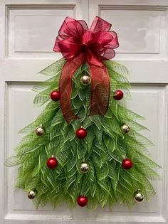 a door decorated with a christmas tree made out of green leaves and red balls, hanging on the front door