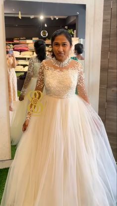 a woman standing in front of a mirror wearing a white dress with sheer sleeves and beading