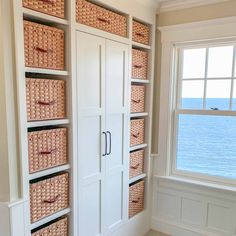 a large white bookcase with baskets on the front and bottom shelves next to a window