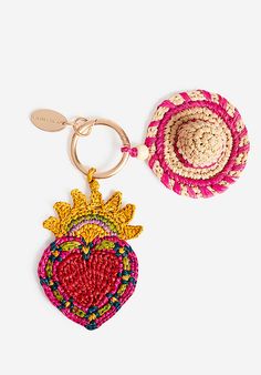 two straw hats and a heart shaped keychain on a white surface, one with a sun motif