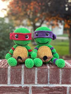 two crocheted teenage mutant turtles sitting on top of a brick wall