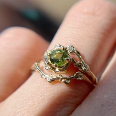 a close up of a person's hand holding a ring with a green stone