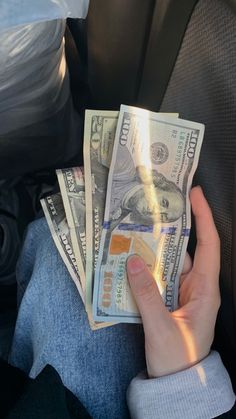 a person holding money in their hand while sitting on the back seat of a car