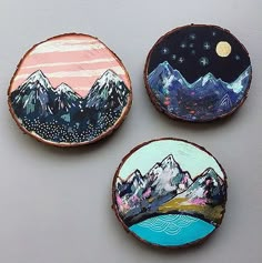 three painted wood slices with mountains on them