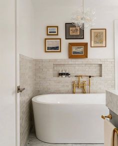 a white bath tub sitting in a bathroom next to a sink and framed pictures on the wall