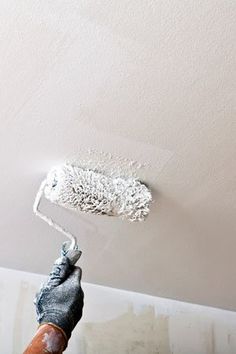 a person is painting the ceiling with white paint and a gray brush in their hand